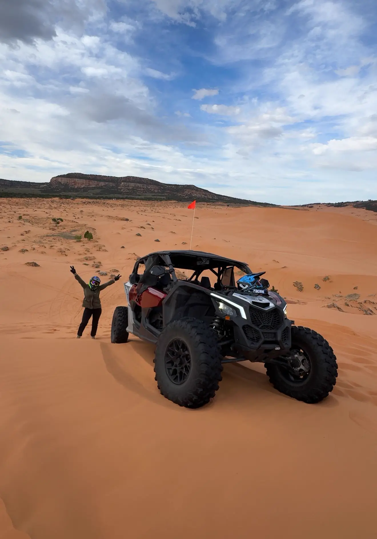 Rider celebrating beside a red Can-Am Maverick on Coral Pink Sand Dunes